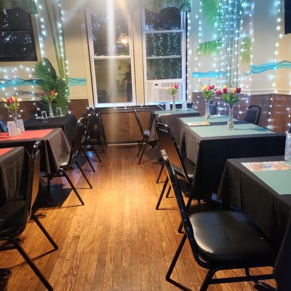 Restaurant dining room with black-draped tables, colorful tulips, string lights, and painted tropical decor.