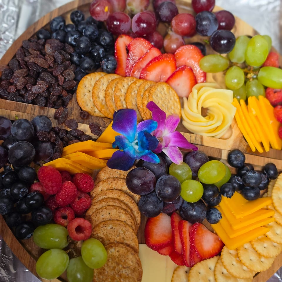 A wooden charcuterie board filled with crackers, various cheeses, fresh berries, grapes, and mango slices.